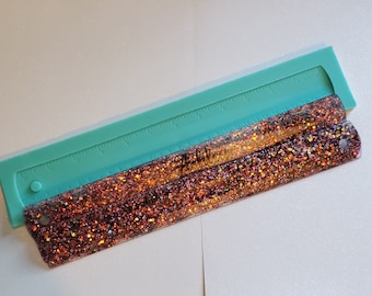 May include: A turquoise ruler with a glittery orange and brown ruler underneath. The glittery ruler has a hole at the end.