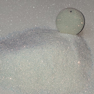 May include: A close-up of iridescent white glitter, with a small round, iridescent white object on top.