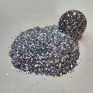 Op de afbeelding: Een hoop iriserende zilveren glitter met een kleine cirkel van dezelfde glitter op de achtergrond.