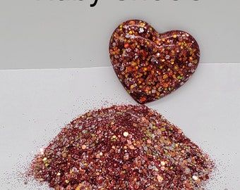 May include: A pile of red, gold, and white glitter with a heart-shaped container of the same glitter. The container is labeled "Ruby Shoe's".