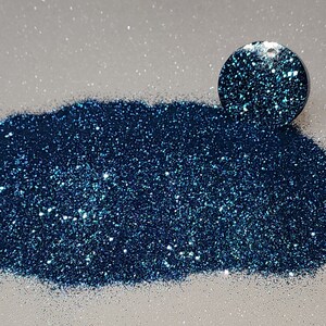 Op de afbeelding: Een hoop turquoise glitter met een iriserende glans. De glitter is los en verspreid over een wit oppervlak.