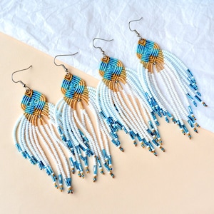 May include: Three pairs of long, beaded earrings with a blue, gold, and white colour scheme. The earrings have a tassel-like design with a geometric pattern at the top.