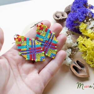 May include: A pair of colourful, geometrically patterned earrings made with macrame and beads. The earrings are in the shape of a teardrop and have a silver hook.