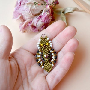 May include: A green, black, white, and gold beaded pendant with a crystal accent. The pendant is hanging from a silver loop.