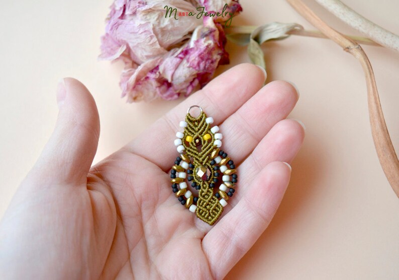 May include: A green, black, white, and gold beaded pendant with a crystal accent. The pendant is hanging from a silver loop.