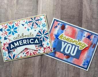 May include: Two rectangular greeting cards. The left card features a white star with the text celebrate AMERICA in blue and gold on a red and blue firework pattern. The right card has a watercolor red and blue background with the text honoring YOU.