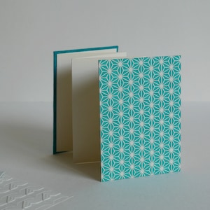 May include: A teal blue card with a white geometric pattern. The card is folded in thirds and has a white interior.
