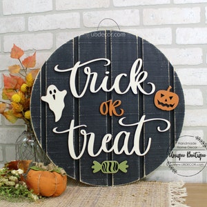 May include: A round wooden sign with the words "trick or treat" written in white script. The sign is decorated with a ghost, a pumpkin, and a candy. The sign is black with white stripes and has a rustic look.