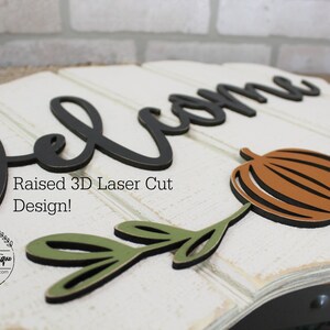 May include: A white wooden sign with the word "Welcome" in black raised 3D letters. The sign also features a brown pumpkin and green leaves, all laser cut. The text "Raised 3D Laser Cut Design!" is printed below the welcome sign. The sign is handmade by Unique Boutique.