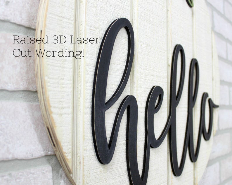 May include: A white wooden round sign with the word "hello" in black raised 3D laser cut lettering. The sign is mounted on a white brick wall. The text "Raised 3D Laser Cut Wording!" is visible in the top left corner of the image.