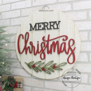 K&ouml;nnte beinhalten: Ein rundes wei&szlig;es Holzschild mit den Worten "Merry Christmas" in schwarzer und roter Schrift. Das Schild hat unten einen gr&uuml;nen und roten Stechpalmenzweig mit Beeren.