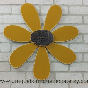 Puede incluir: Una gran margarita amarilla mostaza con un centro blanco y negro. La margarita est&aacute; hecha de madera y tiene un estilo r&uacute;stico, de granja.