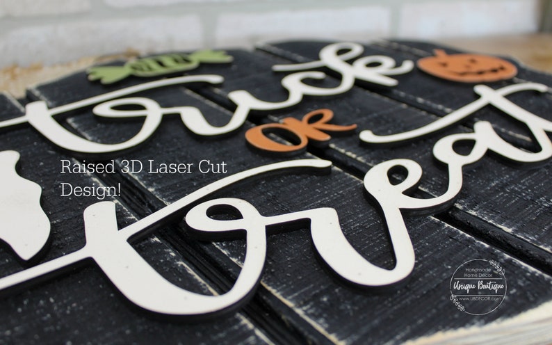 May include: A wooden sign with the words "Trick or Treat" in white raised lettering. The sign is painted black and has a distressed look. The words "or Treat" are in a cursive font. The words "Trick" are in a block font. The sign is decorated with a small pumpkin and a candy corn.