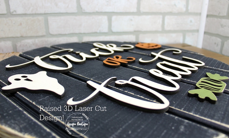 May include: A black wooden sign with the words "Trick or Treat" in white raised letters. The sign is decorated with a white ghost, an orange pumpkin, and a green candy.