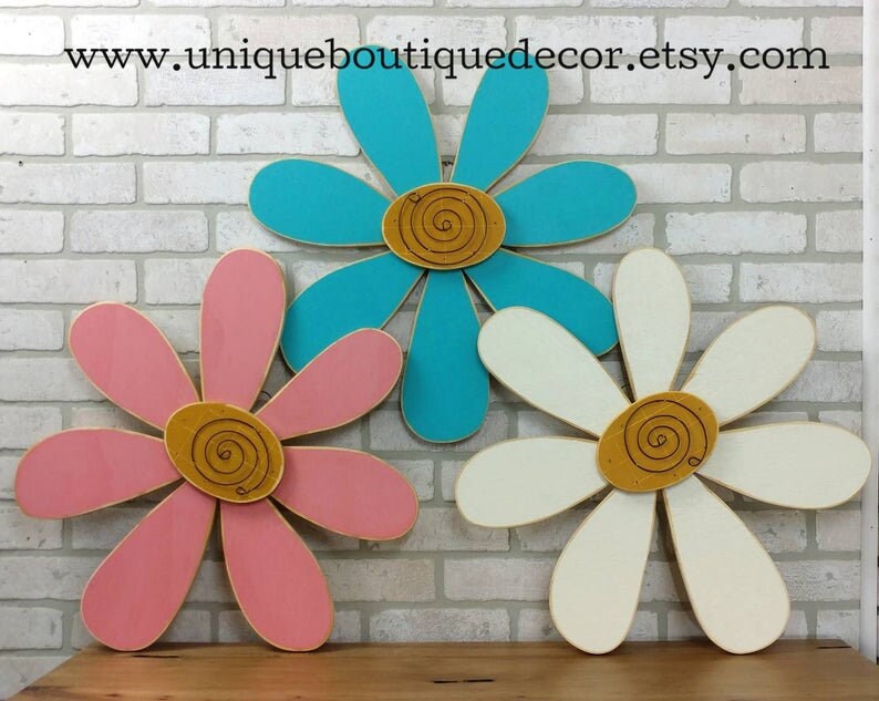 Puede incluir: Tres decoraciones de pared de madera en forma de margarita en rosa, turquesa y blanco con un dise&ntilde;o de espiral dorado en el centro de cada flor.