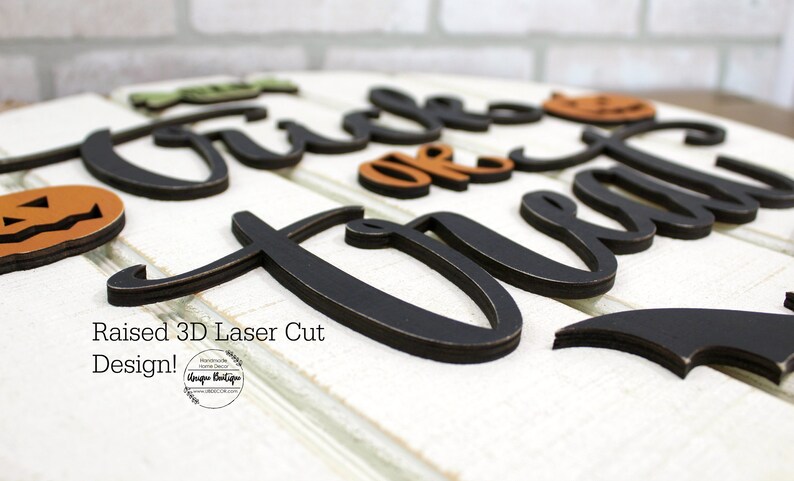 May include: A 3D laser cut wooden sign with the words "Trick or Treat" in black with a distressed finish. The sign is decorated with orange and brown pumpkins and a black bat.