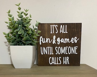 May include: A brown wooden sign with white text that reads "It's all fun & games until someone calls HR".