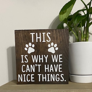 May include: A brown wooden sign with white text that reads "This is why we can't have nice things."  Two white paw prints are above the text.