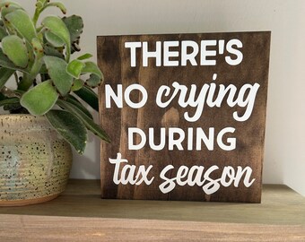 May include: A wooden sign with the text "THERE'S NO crying DURING tax season" in white lettering on a dark brown background.