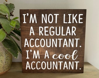 May include: A brown wooden sign with white text that reads "I'm not like a regular accountant. I'm a cool accountant."