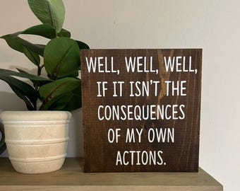 May include: A dark brown wooden sign with white text that reads "WELL, WELL, WELL, IF IT ISN'T THE CONSEQUENCES OF MY OWN ACTIONS."