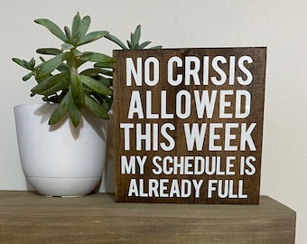 May include: A wooden sign with the text "NO CRISIS ALLOWED THIS WEEK MY SCHEDULE IS ALREADY FULL" in white lettering.