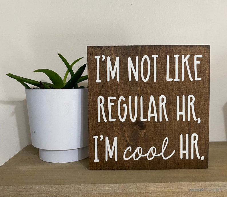 Puede incluir: Un letrero de madera marr&oacute;n con texto blanco que dice "No soy como los RRHH normales. Soy RRHH cool."
