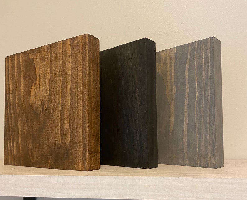 May include: Three wooden blocks in different shades of brown, black, and gray. The blocks are all the same size and shape, and they are arranged in a row from left to right.