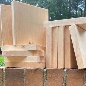 May include: A stack of unfinished wooden squares, some are stacked vertically and some are stacked horizontally. The wood is a light natural color.
