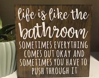 May include: A wooden sign with the text "life is like the bathroom sometimes everything comes out okay and sometimes you have to push through it".