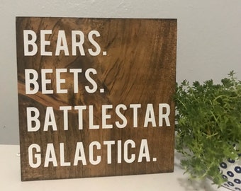 May include: A wooden sign with the text "BEARS. BEETS. BATTLESTAR GALACTICA." in white paint.