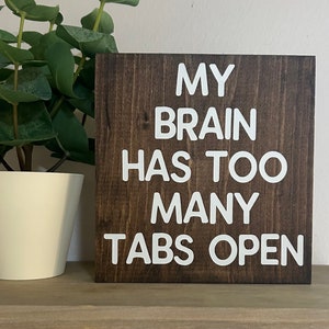 May include: A brown wooden sign with white text that reads "My brain has too many tabs open".