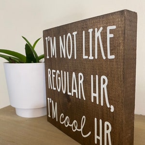 Puede incluir: Un letrero de madera marr&oacute;n con texto blanco que dice "No soy como los RRHH normales. Soy RRHH cool."