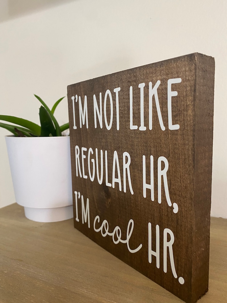 Puede incluir: Un letrero de madera marr&oacute;n con texto blanco que dice "No soy como los RRHH normales. Soy RRHH cool."