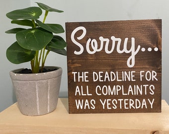 May include: A brown wooden sign with white text that reads "Sorry... The deadline for all complaints was yesterday."