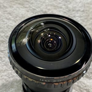 K&ouml;nnte beinhalten: Nahaufnahme eines schwarzen Kameraobjektivs mit Weitwinkeldesign. Das Objektiv hat eine gew&ouml;lbte Glasoberfl&auml;che und einen Metallring mit dem Text "lens made in Japan". Das Objektiv ist f&uuml;r ein breiteres Sichtfeld konzipiert.