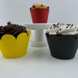 May include: Three cupcake liners, one yellow, one black, and one red, with chocolate and vanilla cupcakes with sprinkles.
