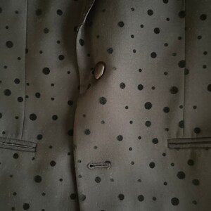 May include: A black blazer with a black polka dot pattern. The blazer has a single button closure and a pocket on the left side.