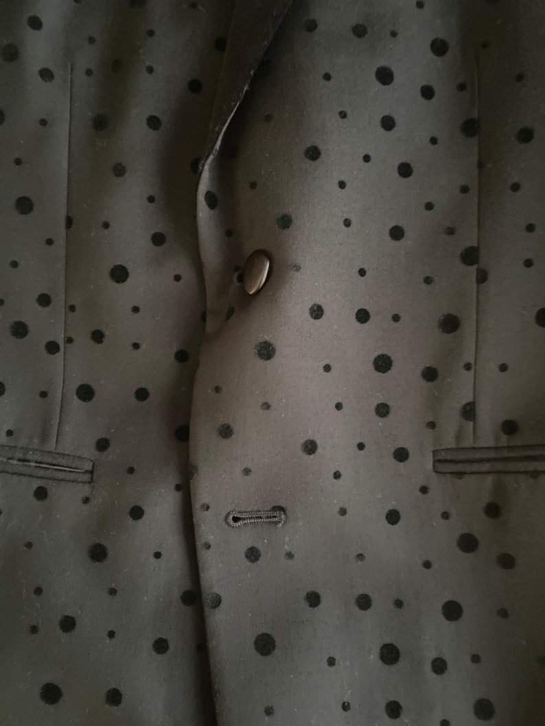 May include: A black blazer with a black polka dot pattern. The blazer has a single button closure and a pocket on the left side.