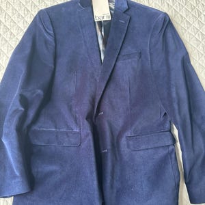 May include: A navy blue blazer with a two-button closure and two front pockets. The blazer has a notched lapel and a tag that reads "bar III". The jacket is hanging on a hanger.