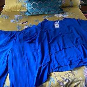 May include: A blue two-piece outfit with a long-sleeved top and pants. The top has a ruffled hem and the pants have a straight leg. The outfit is laid out on a yellow floral bedspread.