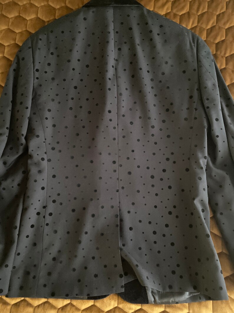 May include: A black blazer with a subtle polka dot pattern. The blazer has a velvet collar and a single button closure.