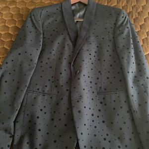 May include: A black blazer with a velvet collar and a black polka dot pattern. The blazer is hanging on a wooden hanger with a Macy's label.