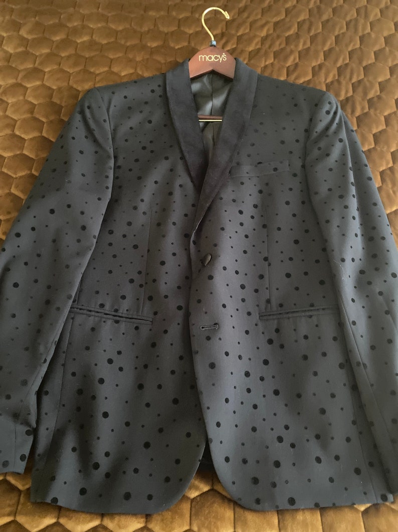 May include: A black blazer with a velvet collar and a black polka dot pattern. The blazer is hanging on a wooden hanger with a Macy's label.
