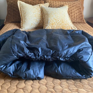 May include: A bed with a dark blue comforter, brown pillows, and a patterned gold and white pillow. The bed has a brown quilted bedspread and a dark blue headboard.
