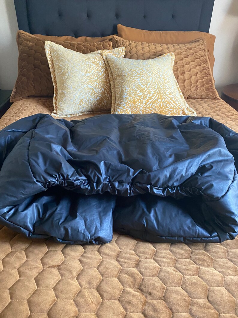 May include: A bed with a dark blue comforter, brown pillows, and a patterned gold and white pillow. The bed has a brown quilted bedspread and a dark blue headboard.
