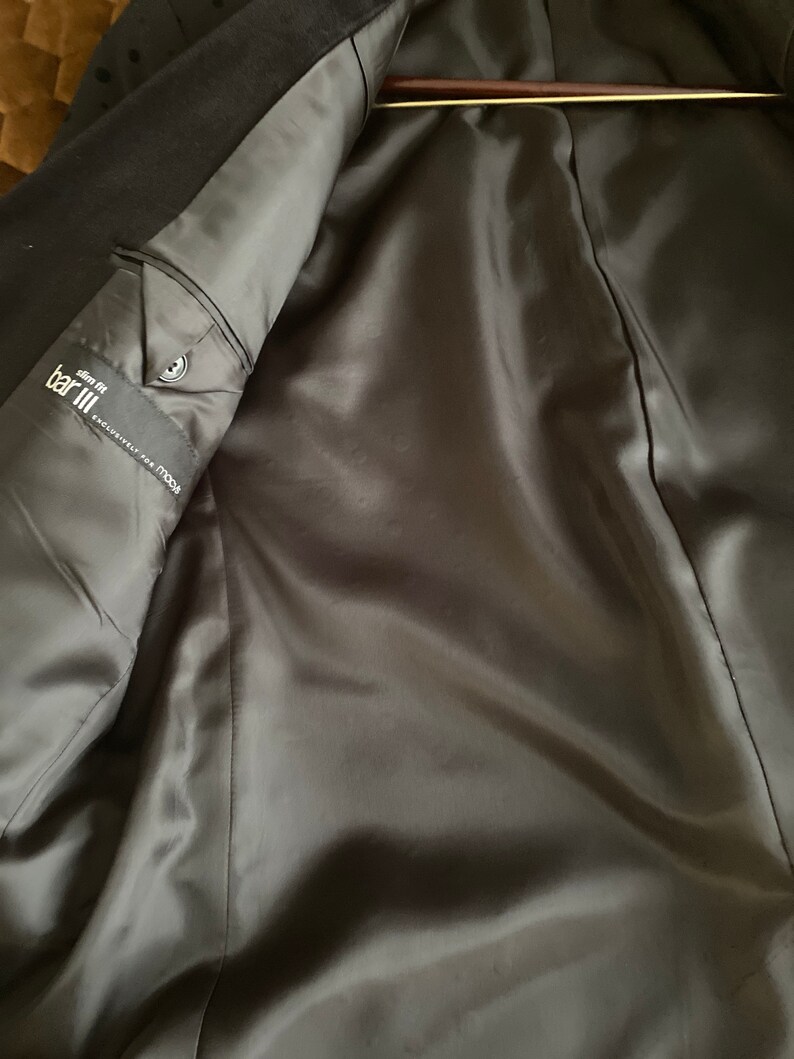 May include: The inside of a black blazer with a satin lining. The label reads "Bar III, Slim Fit, Exclusively for Macy's".