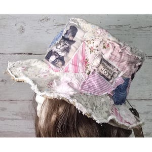 May include: A patchwork bucket hat featuring various fabric scraps in shades of pink, white, and blue. The hat displays a printed image of a cat wearing a top hat and a rectangular fabric patch with the printed text Choose JOY.