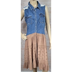 May include: A sleeveless dress featuring a blue denim bodice with a button-down front, two chest pockets, and white lace trim on the shoulders. The lower portion is a tan skirt with horizontal bands of intricate eyelet embroidery and a ruffled hem.