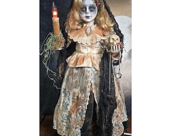 May include: A doll with blonde hair and pale skin wearing a cream-colored dress with lace overlays and a black lace veil. The doll holds a lit orange candle in one hand and a small skull with a pocket watch in the other, adorned with red roses.